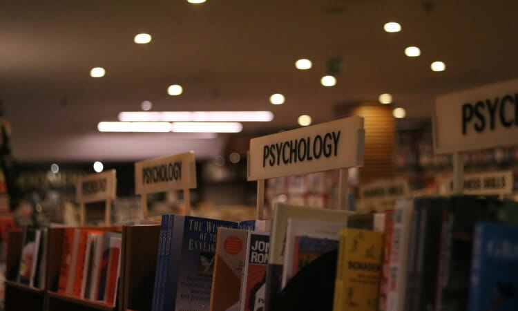 Bookshelves filled with psychology books, with signs indicating the section. Bright ceiling lights illuminate the scene.