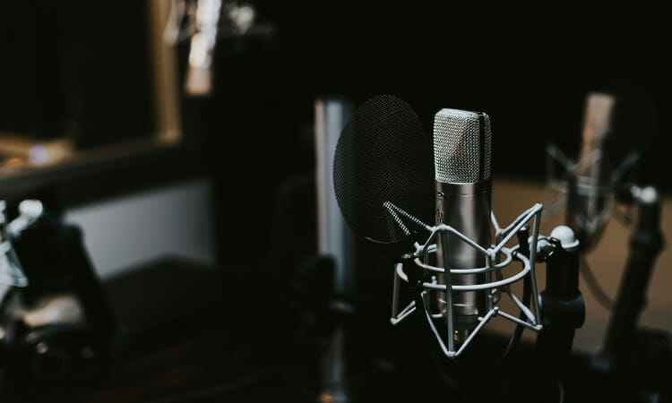 A close-up of a professional microphone with a pop filter in a recording studio, surrounded by other audio equipment.