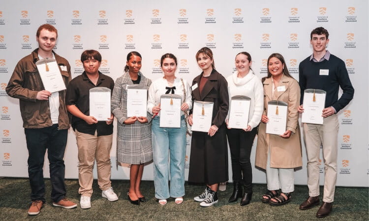 Eight people stand in a row holding certificates, posing for a photo.