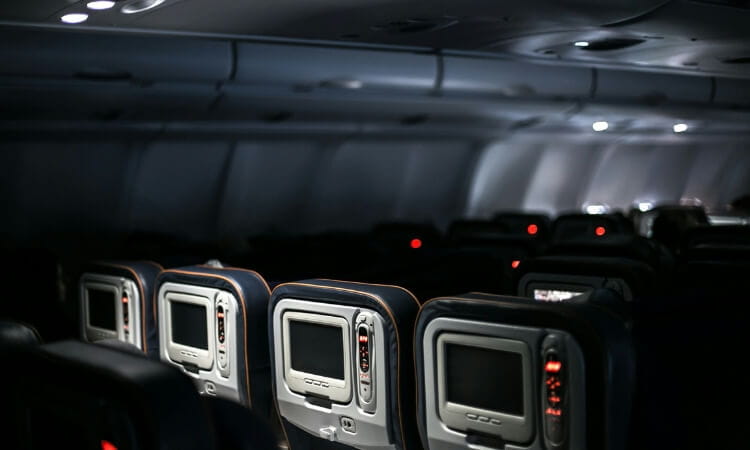 Dimly lit airplane cabin showing several rows of empty seats with individual seat-back screens.
