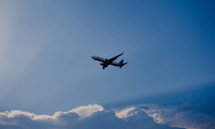 A commercial airplane is flying above white clouds against a clear blue sky.