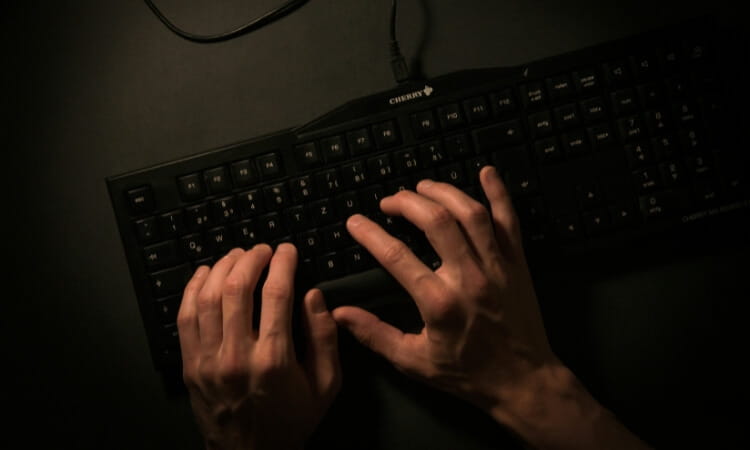 A pair of hands typing on a black QWERTY computer keyboard, photographed from above against a dark background.