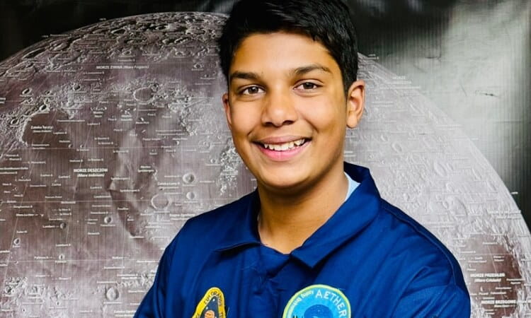 A young person wearing a blue uniform with space-themed patches stands in front of a detailed image of the moon.