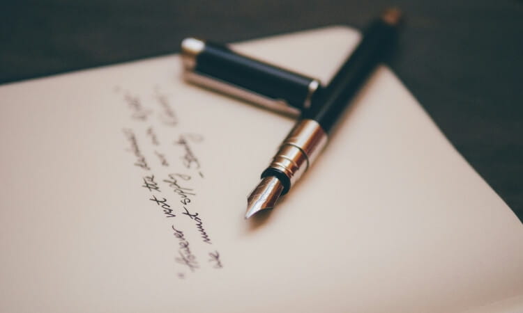 A black fountain pen with its cap off rests on a piece of paper with handwritten text.