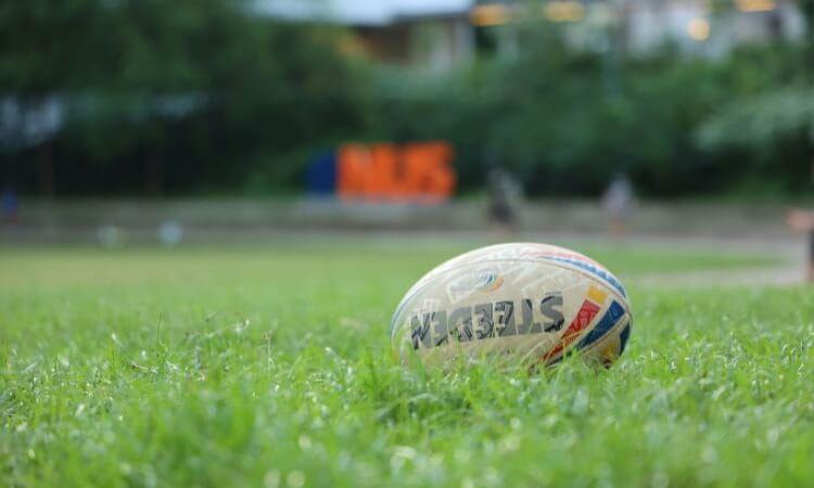 A rugby ball rests on green grass with blurred outdoor background.