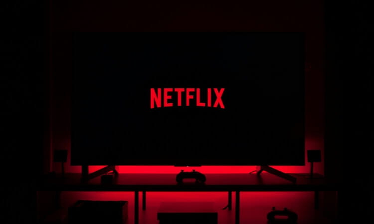 A television screen displays the red Netflix logo against a dark background, with red backlighting illuminating the area beneath the screen.
