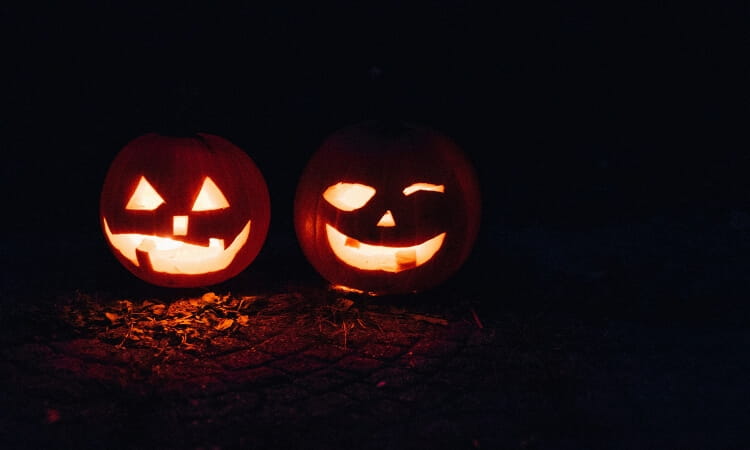 Two carved jack-o’-lanterns with candlelight inside are sitting on the ground in the dark.