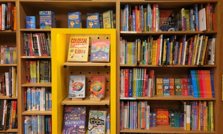 Bookshelves filled with colorful children's books and educational materials; a yellow display shelf holds featured books in the center.