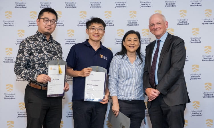 Four people stand in front of a University of Southern Queensland step-and-repeat backdrop, with two holding certificates and all smiling at the camera.