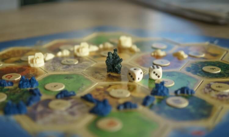 A Settlers of Catan game board with playing pieces, dice showing 4 and 3, and resource tokens on hexagonal tiles.