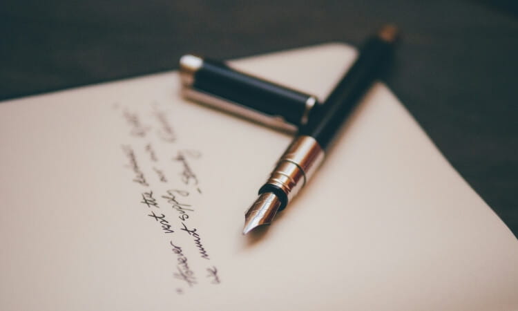 A black fountain pen with a silver trim rests on a piece of paper with handwritten text; the pen cap is placed nearby.
