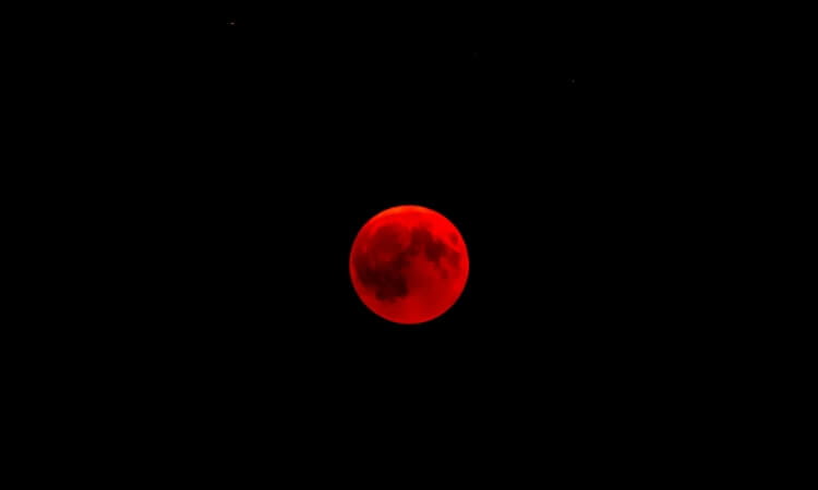 A bright red moon is centered against a black sky during a lunar eclipse.