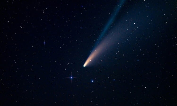 A bright comet with a long tail travels through a star-filled night sky.