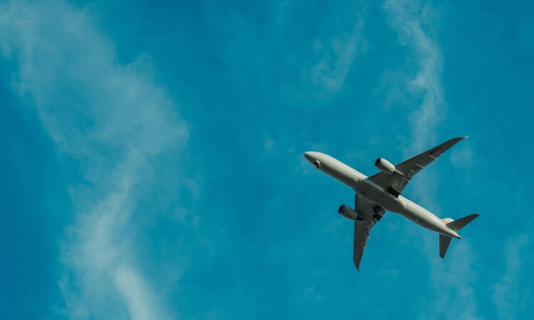 A commercial airplane flies overhead against a clear blue sky with scattered clouds.