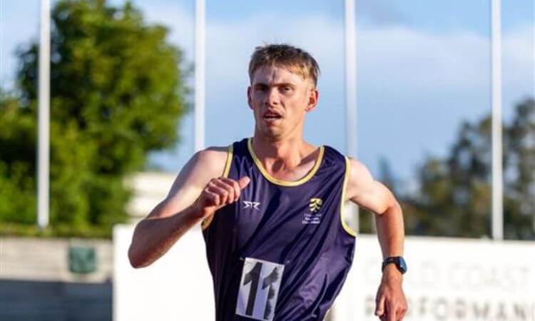 A male athlete wearing a navy blue running vest and race bib number 11 runs outdoors during a track event.