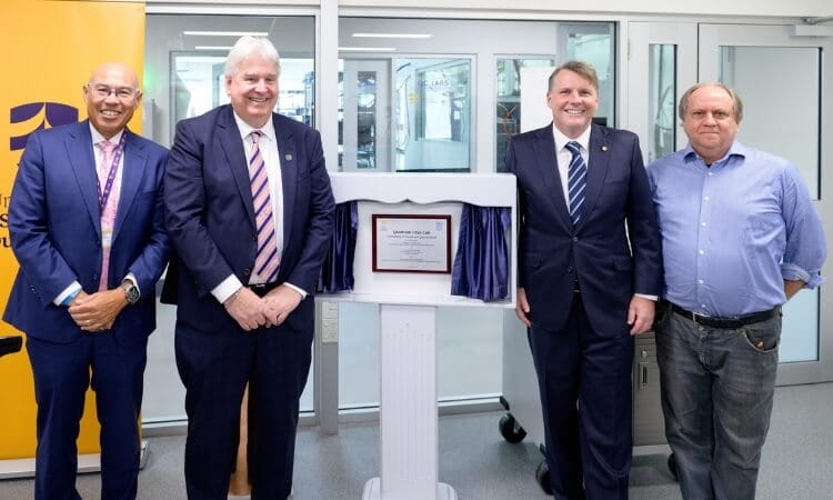 Four men in business attire stand beside a plaque mounted on a stand, posing for a photo in a modern indoor setting.