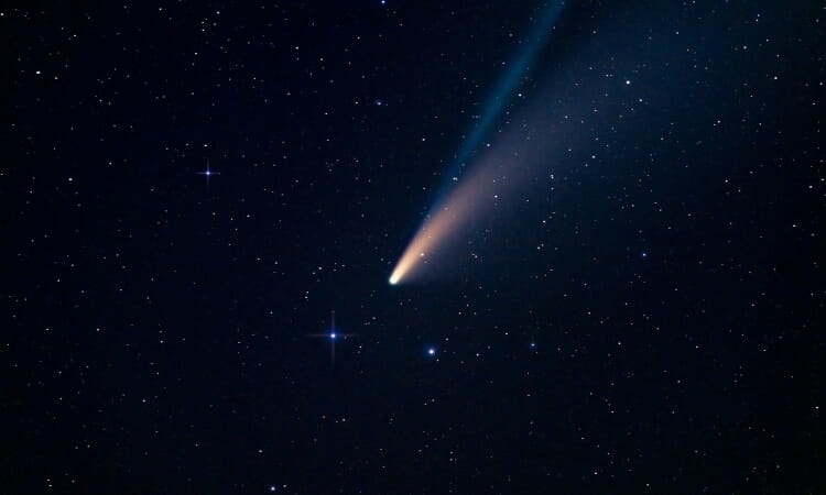 A bright comet with a glowing tail moves across a star-filled night sky.