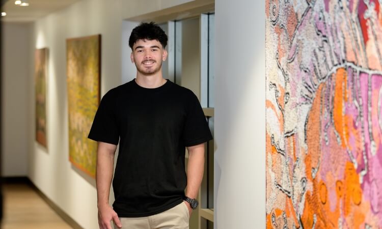 A person in a black t-shirt and beige pants stands in a hallway with colorful abstract paintings on the walls.