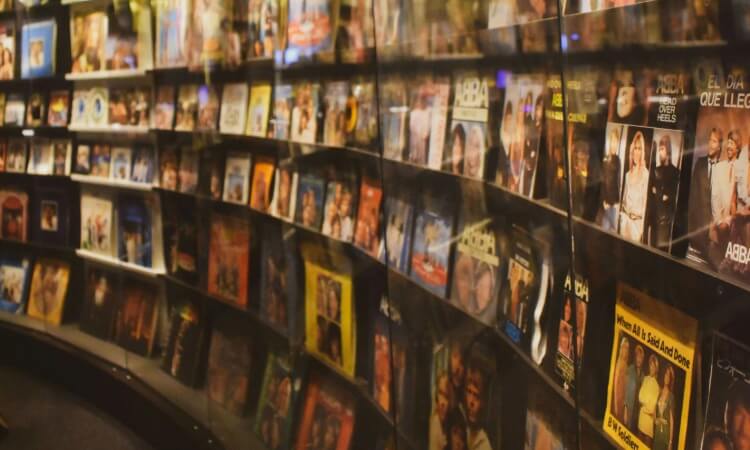 A curved wall display features numerous vinyl album covers arranged in rows, showcasing a variety of artists and music genres behind a reflective glass surface.