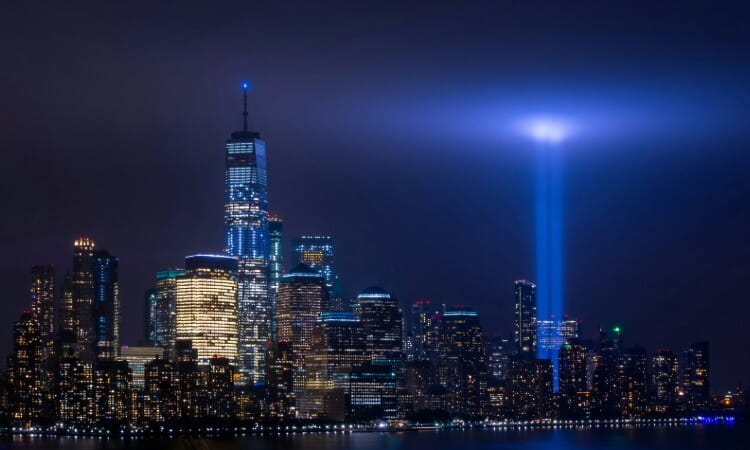 New York City skyline at night with two blue beams of light projected into the sky, commemorating the World Trade Center.