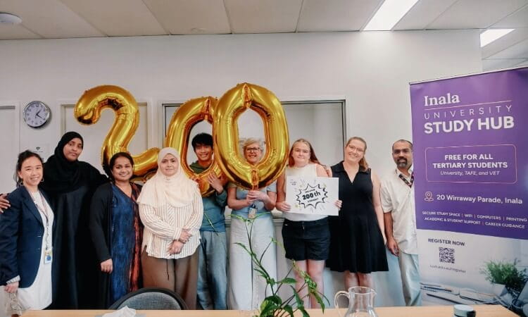 A group of people stand indoors holding gold “200” balloons and a sign, next to a banner for Inala University Study Hub.