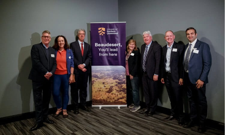 Seven people standing in a row in front of a University of Southern Queensland banner in a room.