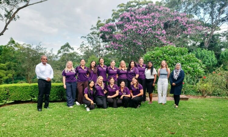 A group of fifteen people posing for a photo on a grassy lawn in front of flowering trees.