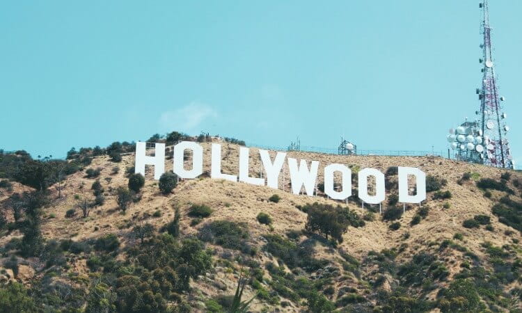 The Hollywood sign on a grassy hillside with a tall radio tower to the right.