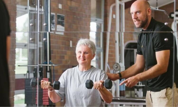 a man helping an elderly woman to exercise in the exercise and sports science clinic