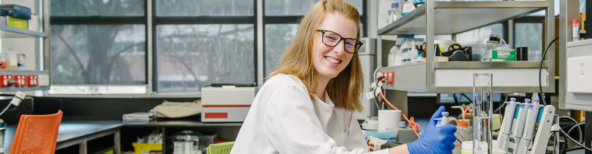 Female laboratory technician smiling at the camera while working in a science lab.