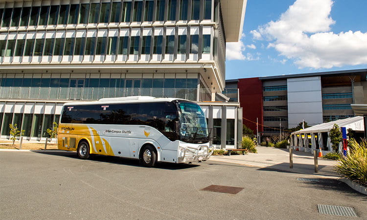 A white and yellow bus parked in front of modern buildings under a clear blue sky.
