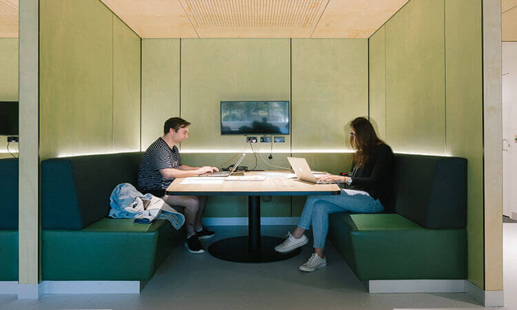 Two individuals working on laptops at a modern booth with integrated lighting and a shared table.