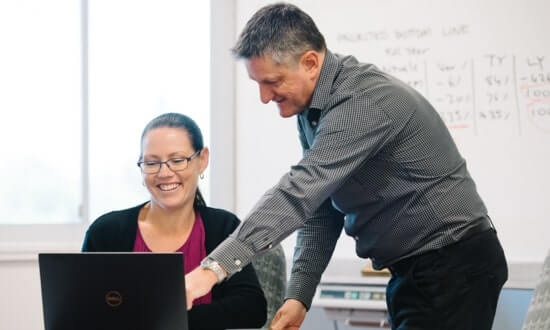 Two colleagues discussing work on a laptop in an office setting.