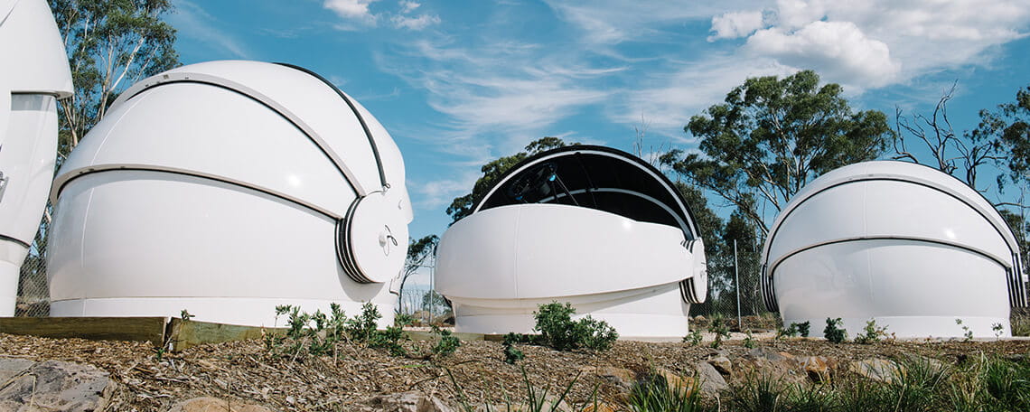 Three white, dome-shaped observatory structures under a blue sky with scattered clouds at UniSQ's Mt Kent Observatory.