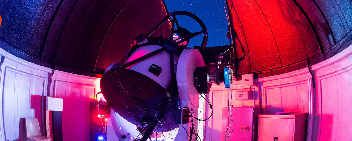 An observatory interior with a telescope under a red-lit dome at night.