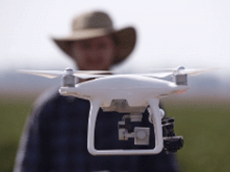 Person in a cowboy hat holding a drone with a camera in the foreground.