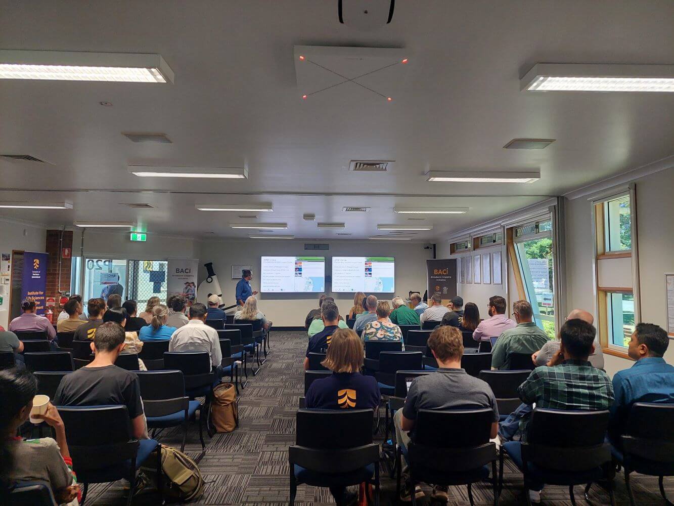 People seated in a conference room facing a presenter with a projection screen at the front.