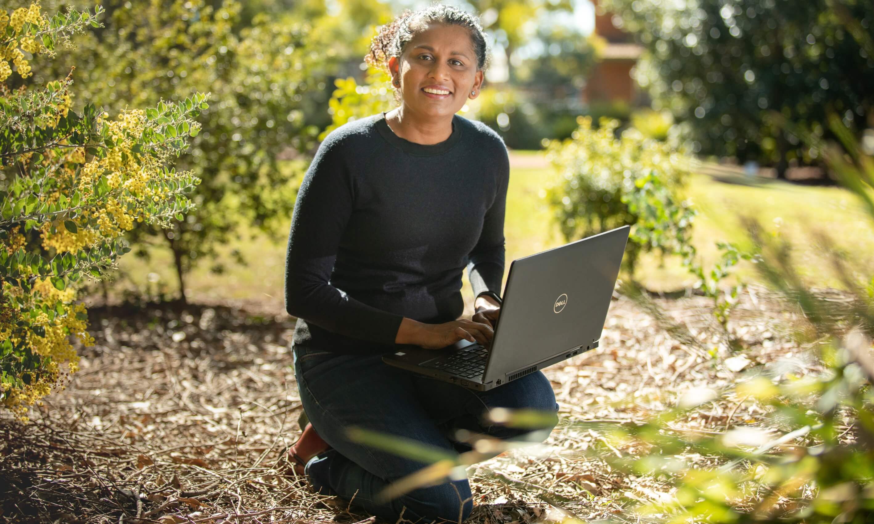 a woman kneeling down in the scrub with a laptop