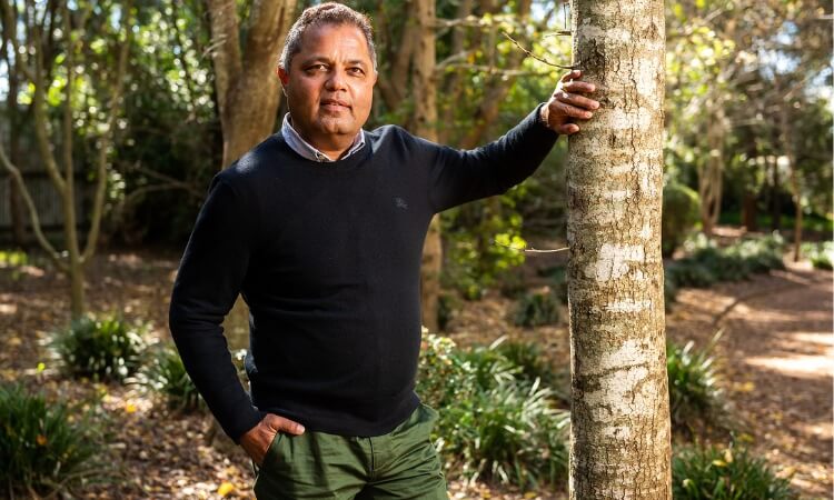 a man standing beside a tree looking at the camera