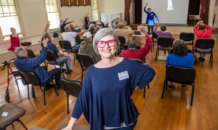woman standing in front of elderly exercise class smiling