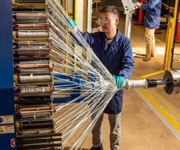 A worker inspects a bundle of elongated metallic parts in a manufacturing setting.
