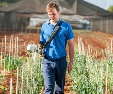 A man walks through a garden carrying a small device, possibly for measuring or tending plants.