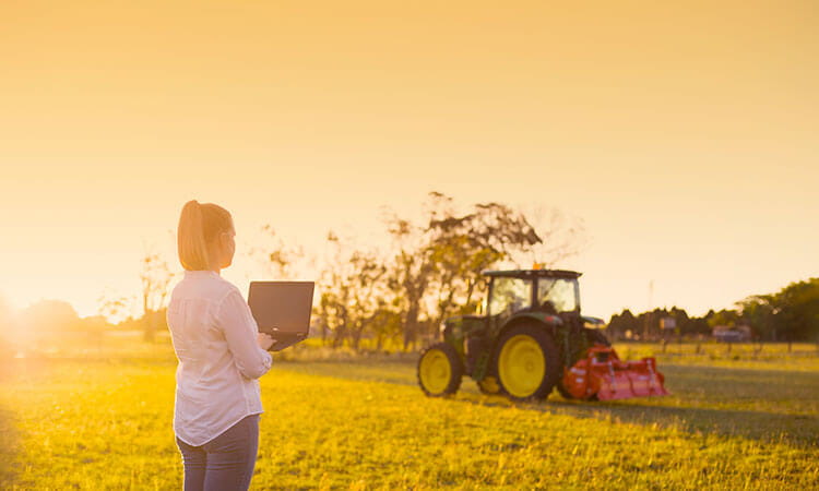 Young farmer with laptop standing near John Deere tractor.