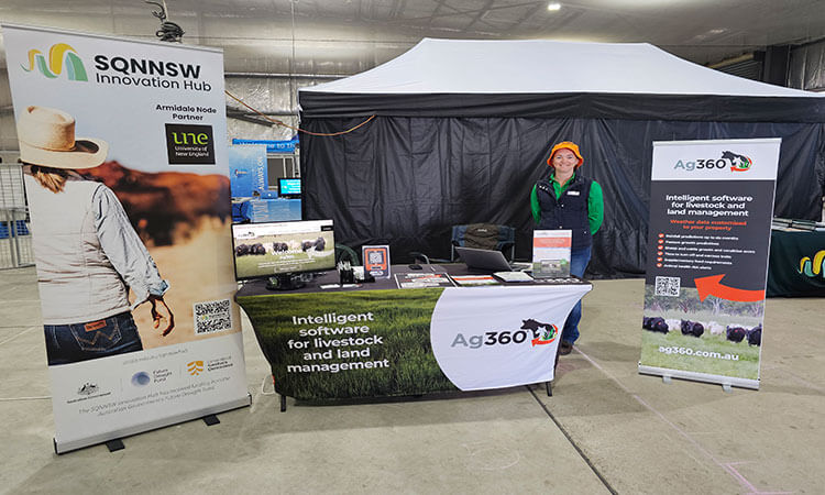 A promotional booth for Ag360 with banners, a table with brochures, and a person standing behind it, set inside a large indoor area.