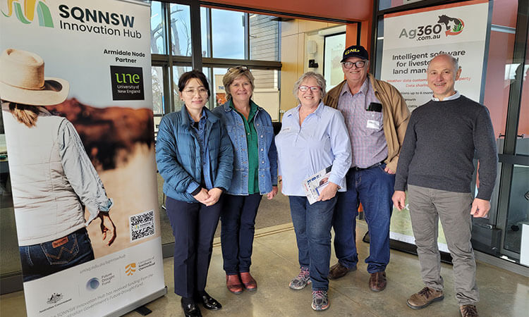 Five people standing indoors, smiling, between two banners promoting innovation and agriculture software.