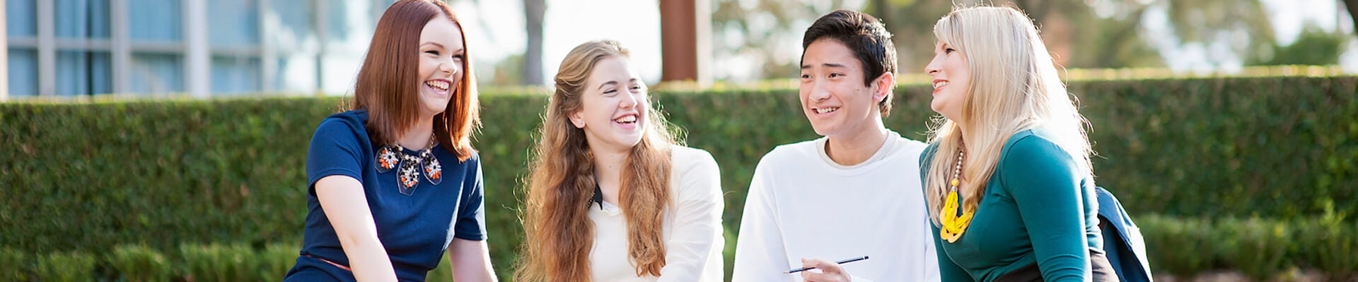 Four young adults sitting outdoors, engaging in conversation and smiling.