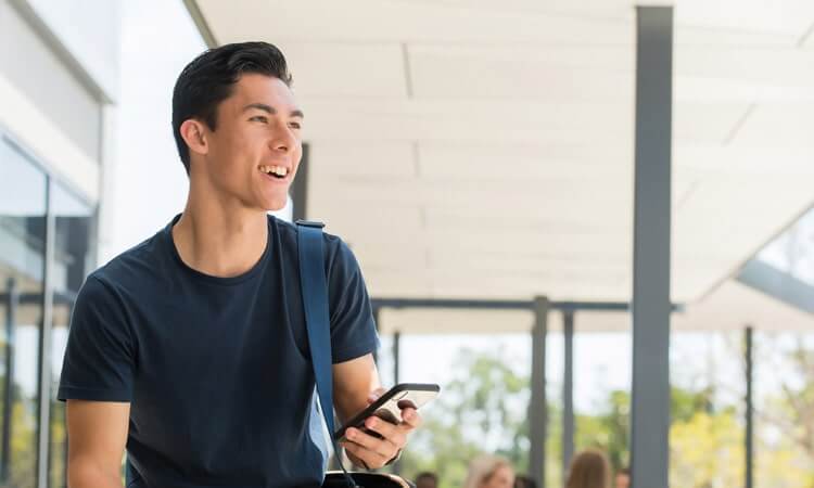 Young man smiling while holding a smartphone outside a building.