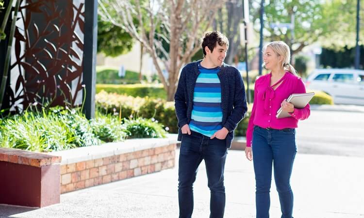 Two people walking and conversing on a sunny day on a campus-like setting.