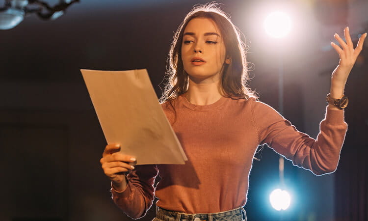 Actor standing on stage with script in hand.