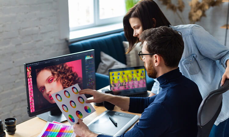 Two people standing around a desk looking at advertising creative on computer screen.